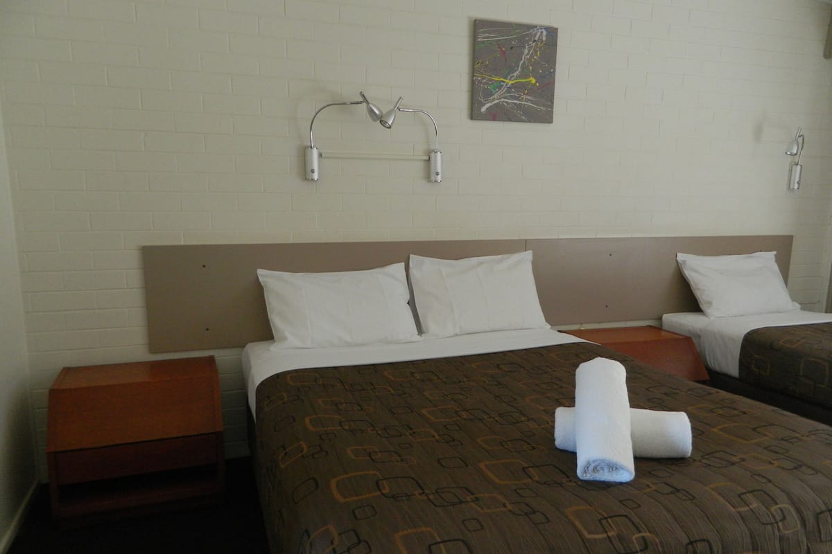 Una habitación de hotel con dos camas, sábanas blancas, colcha marrón con estampado y una sola obra de arte en la pared.