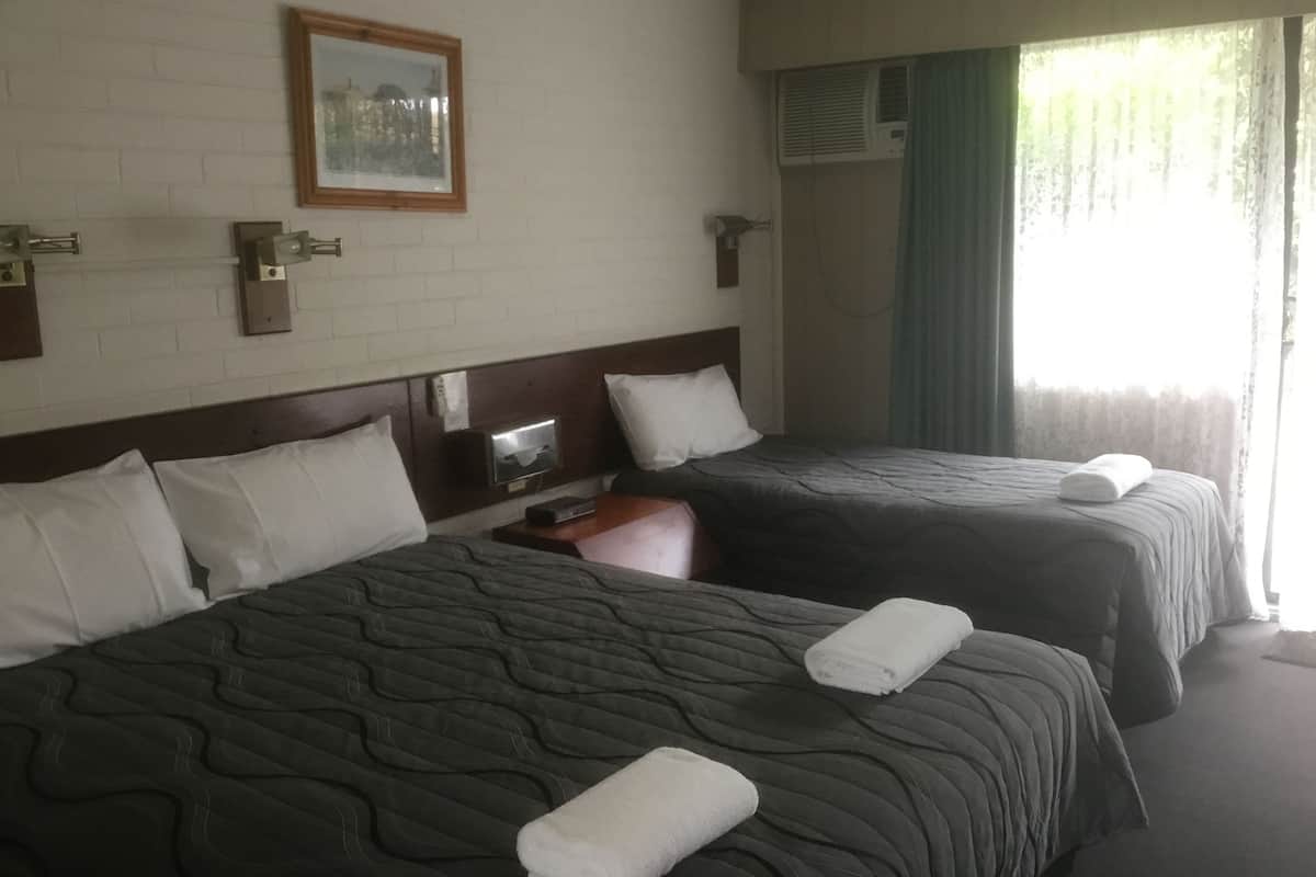 Habitación de hotel con dos camas, un cuadro en la pared, un equipo de aire acondicionado y una ventana con cortinas.