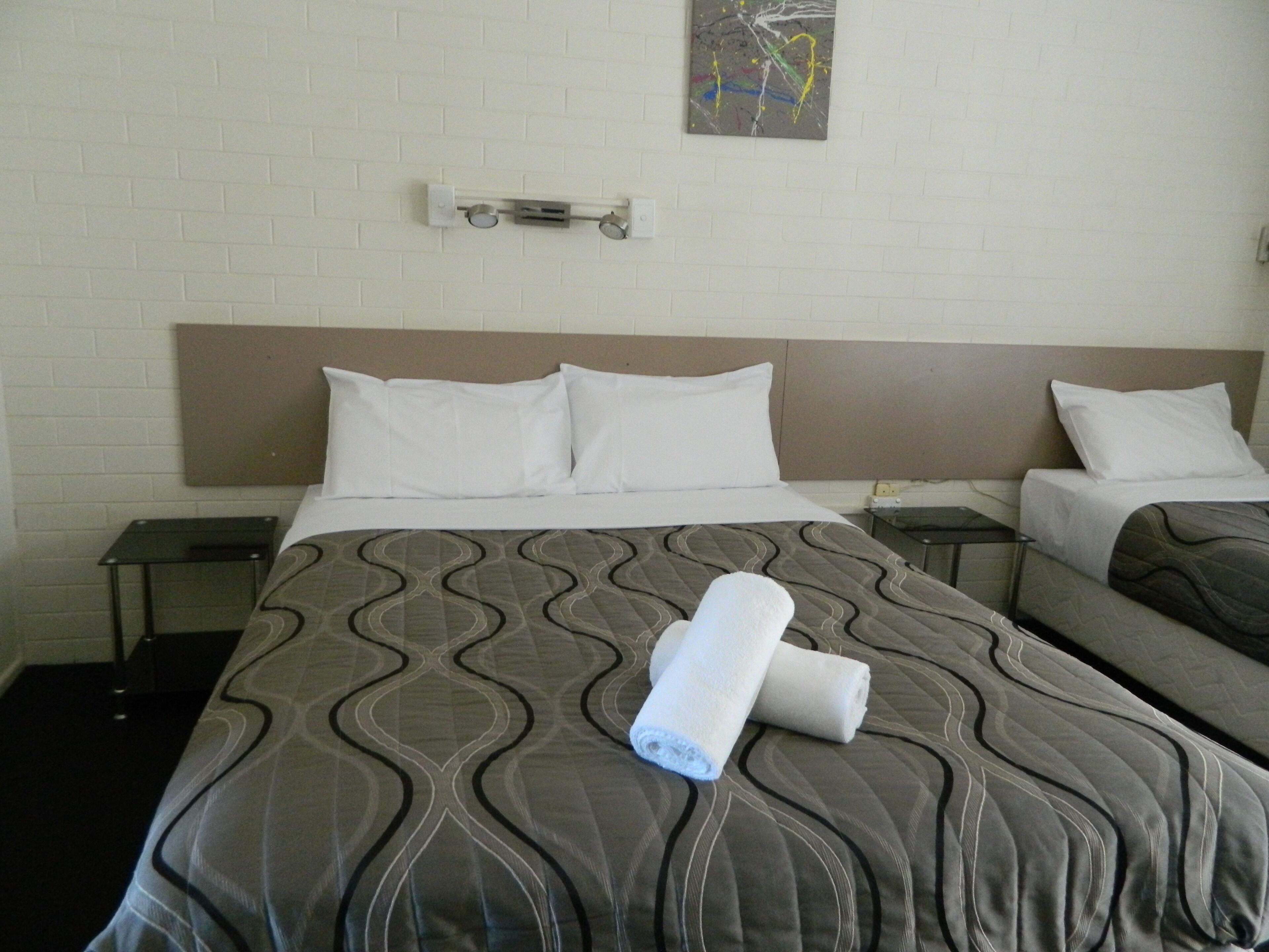 Une chambre d’hôtel avec un lit, deux tables de chevet, une lampe fixée au mur et un tableau.