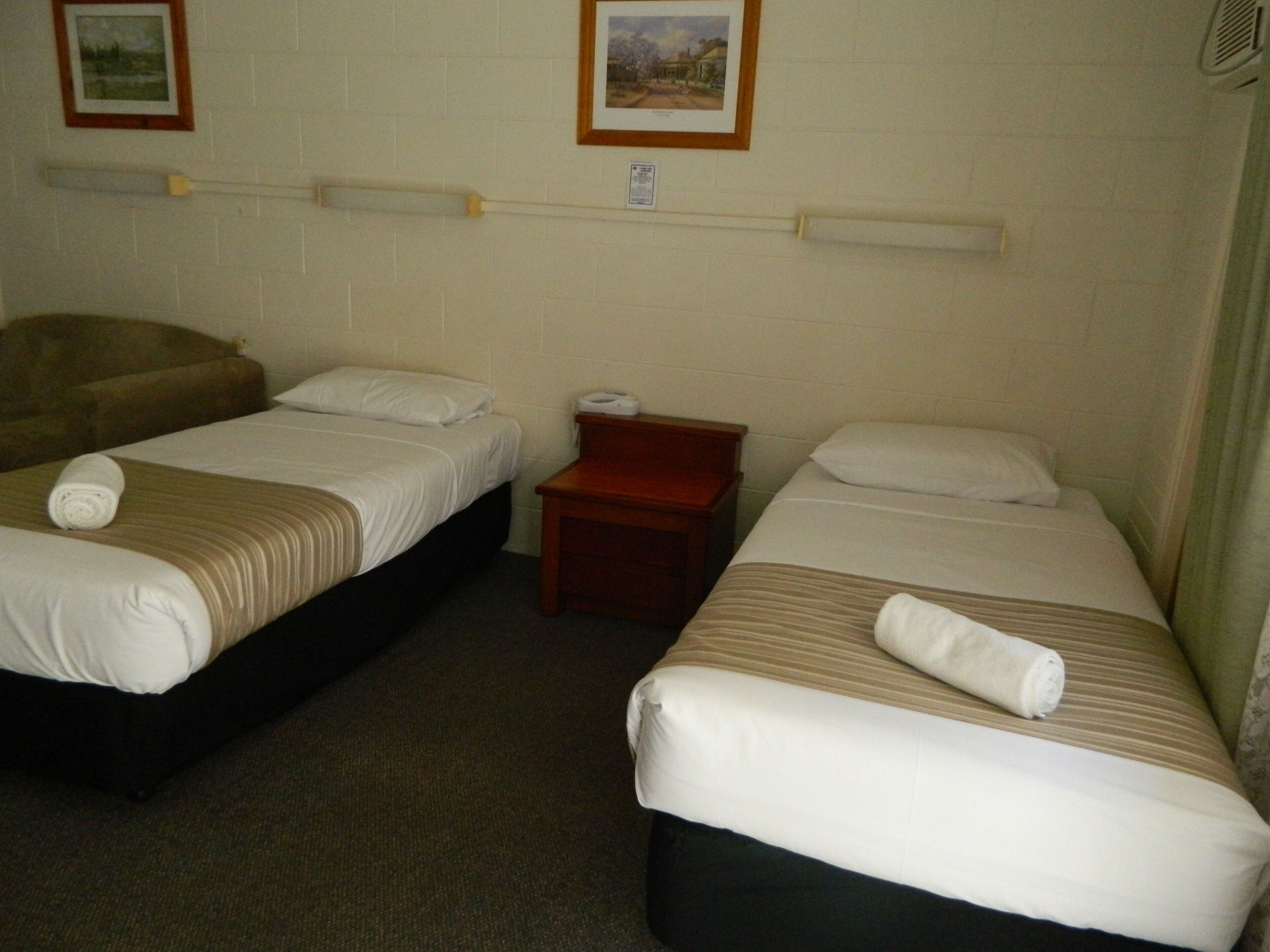 A hotel room with two single beds, each with a rolled towel, a wooden nightstand, and a small table.
