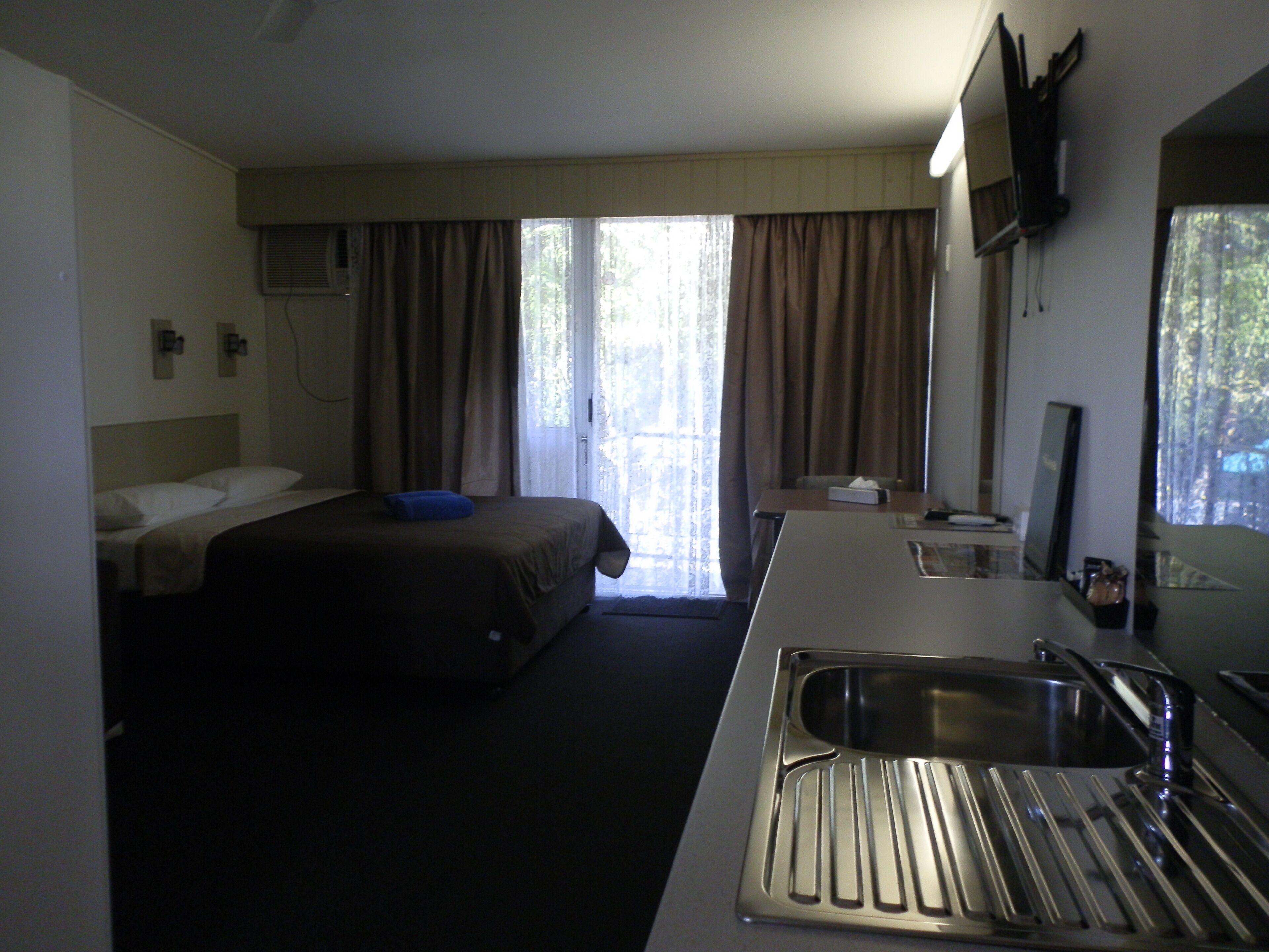 A hotel room with a bed, a desk with a sink, a mirror, and a TV on the wall.