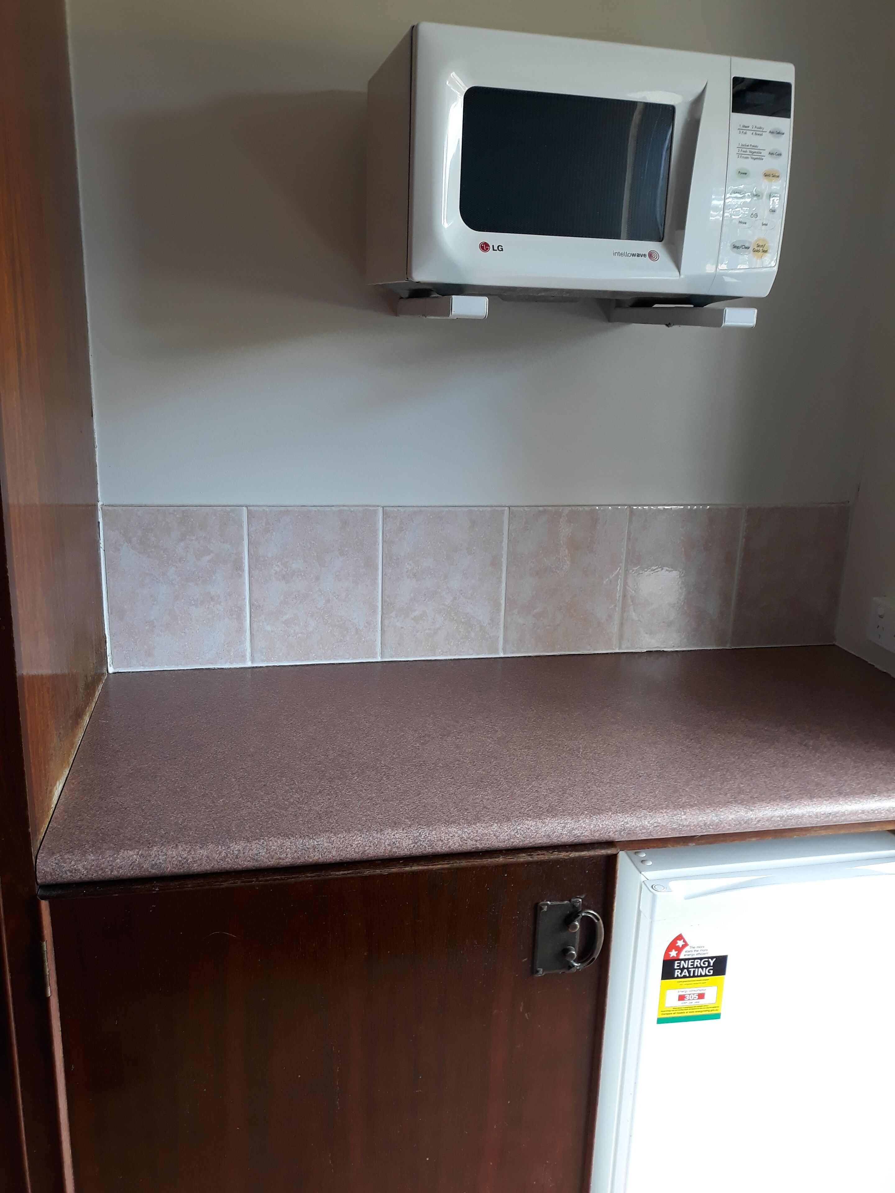 Una cocina con un microondas en un estante, una encimera marrón y un refrigerador con etiqueta de eficiencia energética.