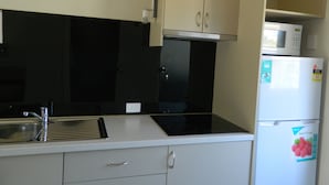 Una cocina compacta con lavamanos, estufa, microondas y refrigerador.