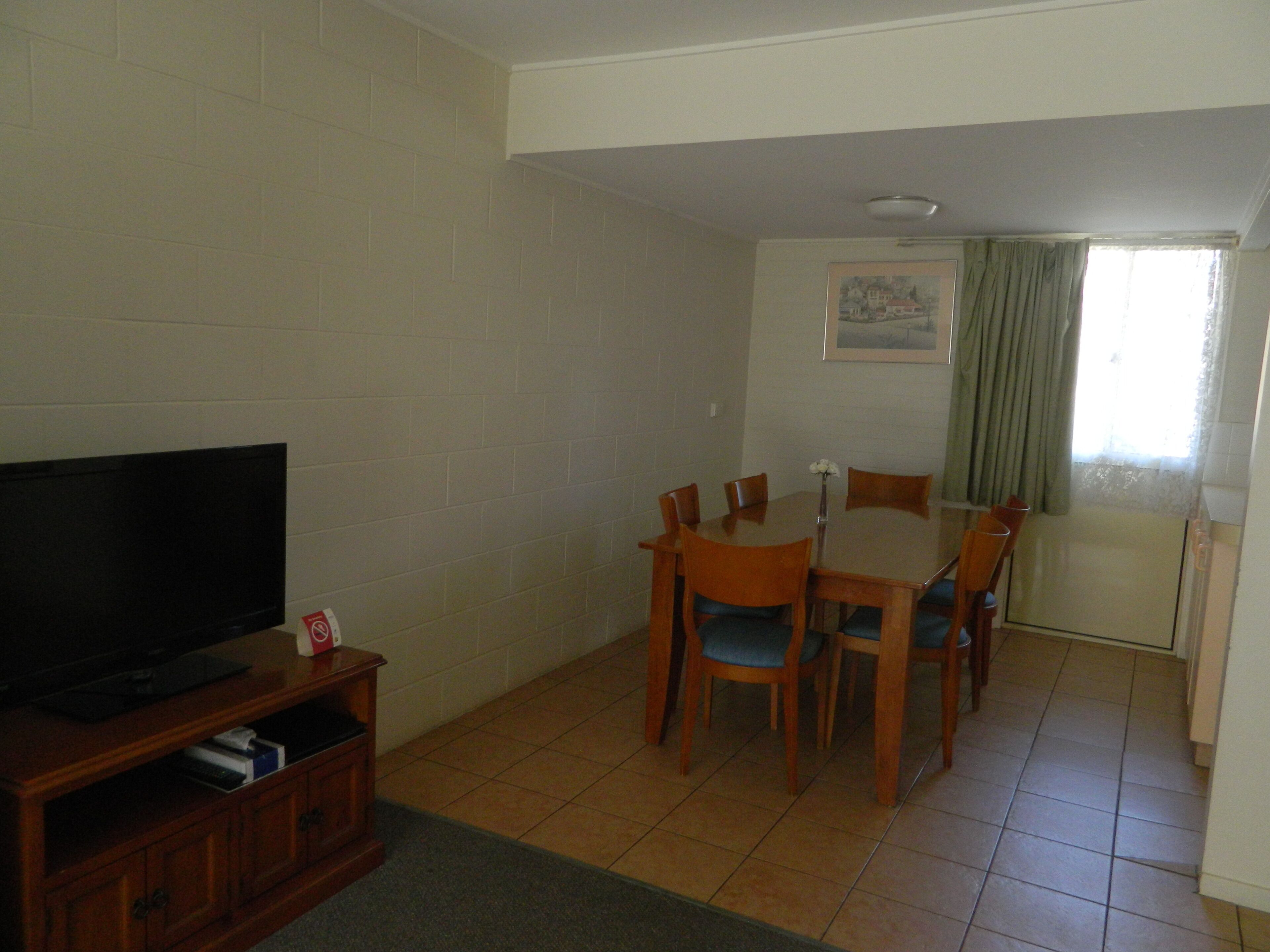 A living room with a flat-screen TV, wooden dining table, and chairs.
