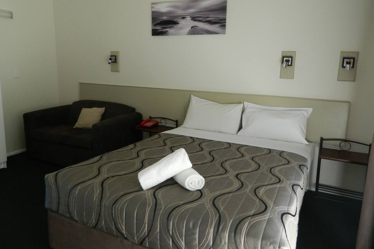 Habitación de hotel con cama, sofá, un cuadro en la pared y un teléfono en la mesita de noche.