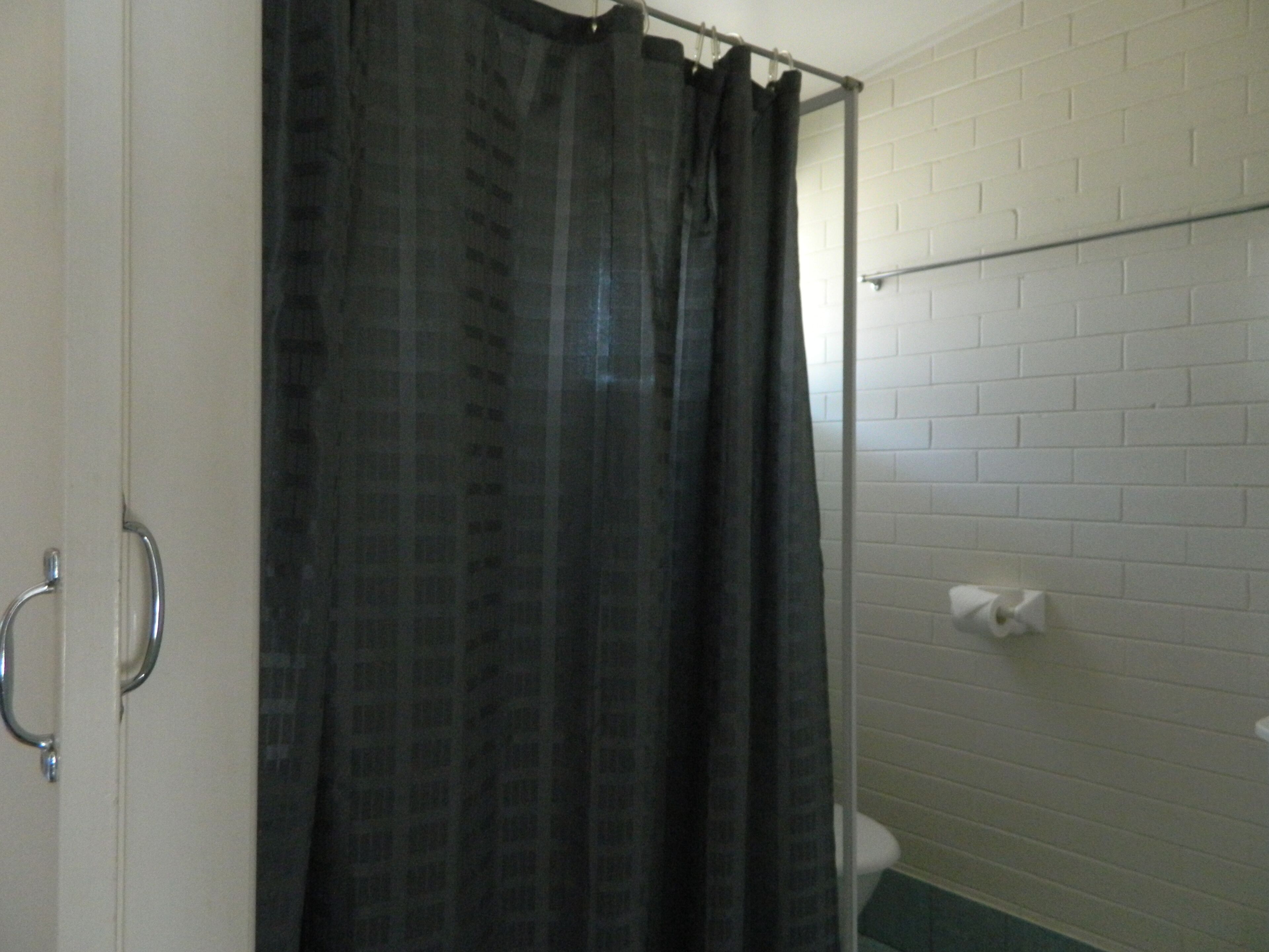 A bathroom with a white tiled wall, a black shower curtain, and a white toilet.