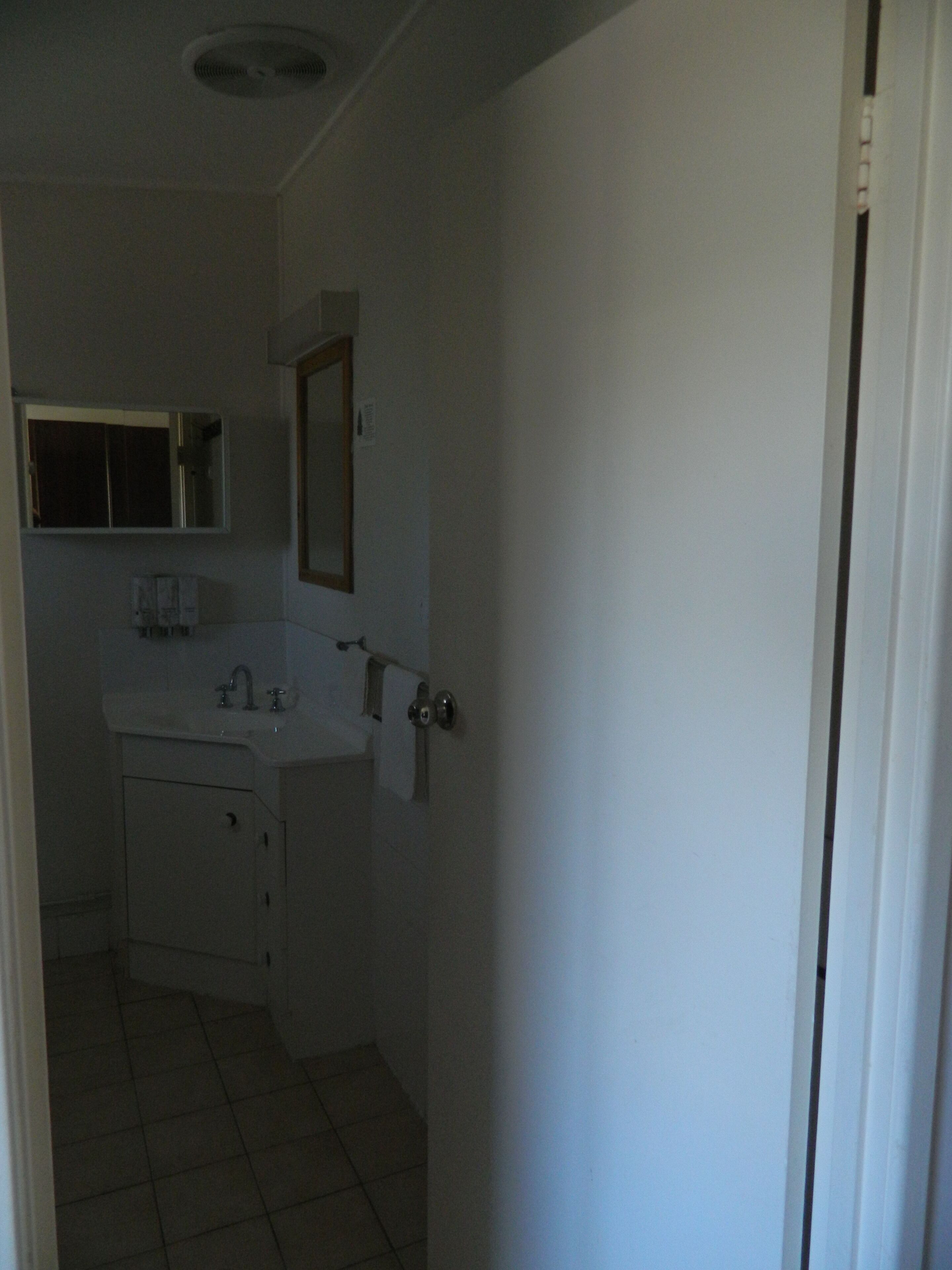 A small, dimly lit bathroom with a white sink, mirror, and cabinets.