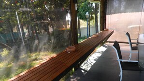 Un banco de madera con una planta en maceta a un lado, con vistas a un jardín con árboles y una valla.