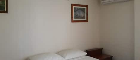 Habitación de hotel con una cama individual, una mesita de noche, un cuadro en la pared y un equipo de aire acondicionado.