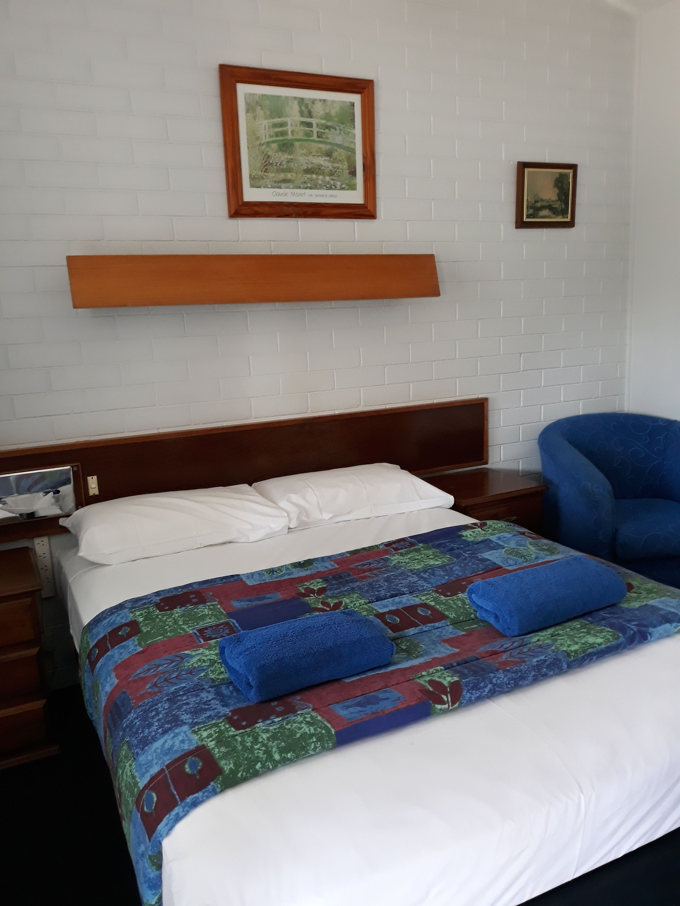 A neatly made bed with a colorful quilt, a wooden headboard, and a blue chair.