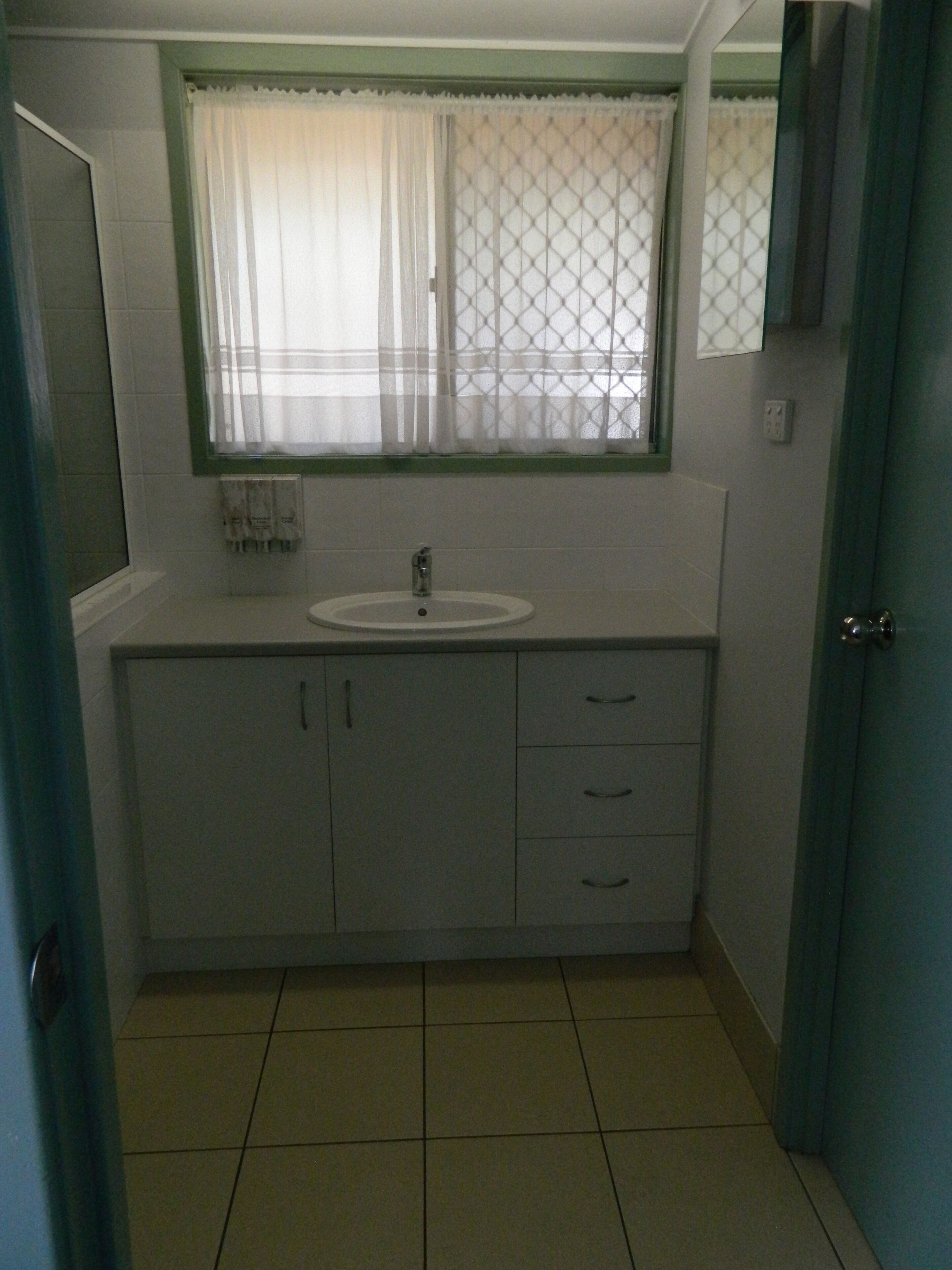 Un bagno piccolo con un lavandino, una finestra con tenda e una porta.