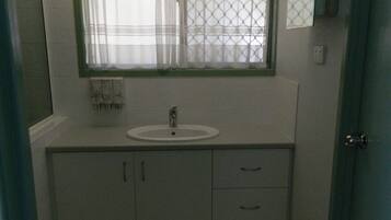 Un baño pequeño con lavamanos, una ventana con cortina y una puerta.