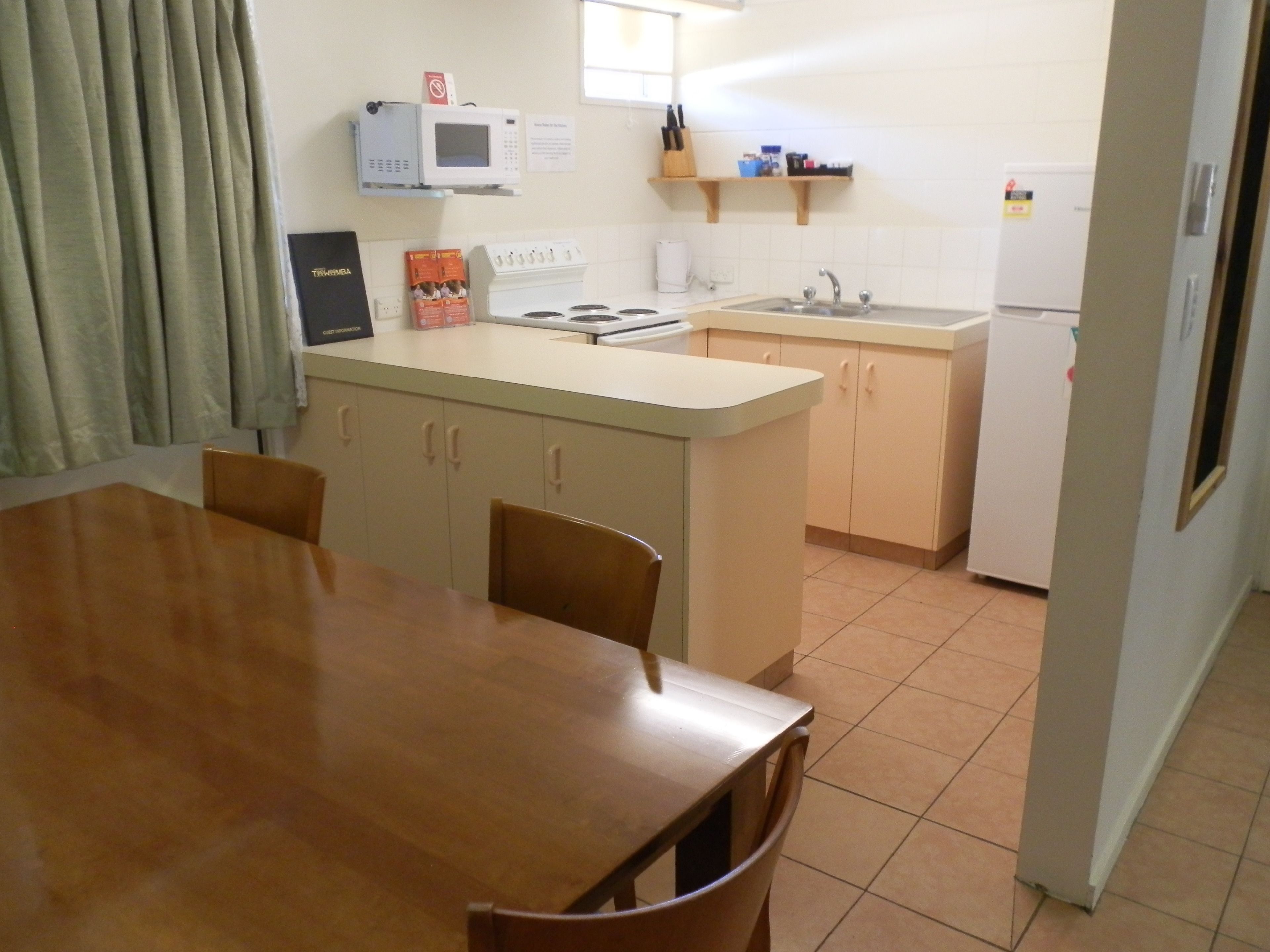 Cocina compacta con una mesa y sillas, microondas, estufa, lavaplatos y refrigerador.