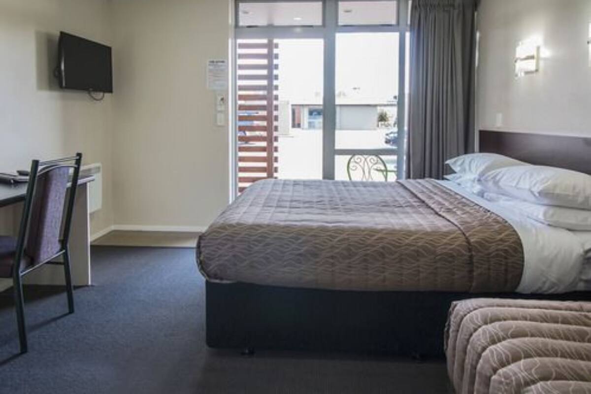 A hotel room with a bed, a desk, a chair, a TV, and a view of the outside.