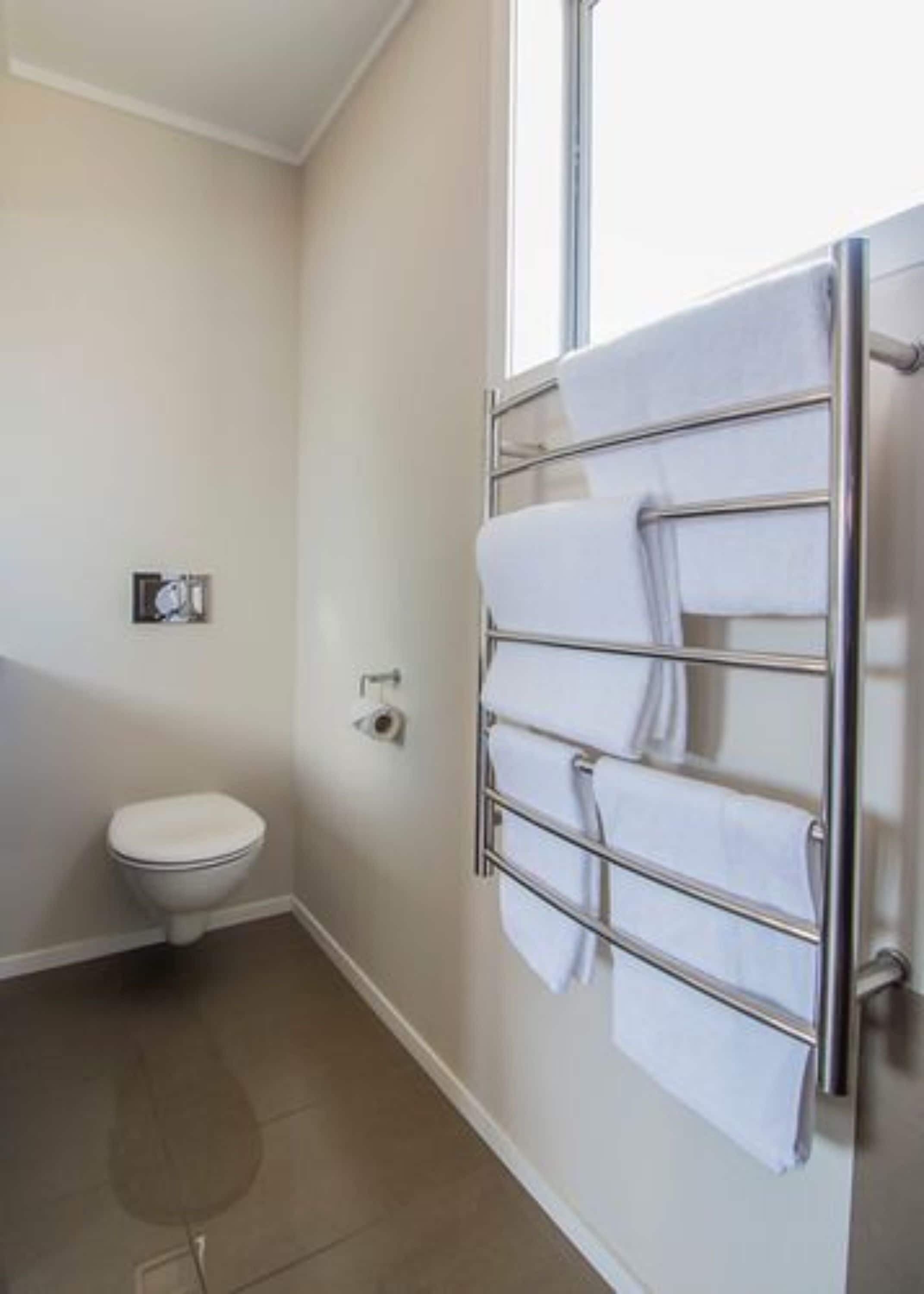 A bathroom with a toilet, a towel rack with multiple towels, and a window.