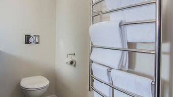 A bathroom with a toilet, a towel rack with multiple towels, and a window.
