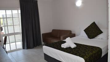 A hotel room with a bed, a brown chair, a large window with curtains, and a ceiling light.