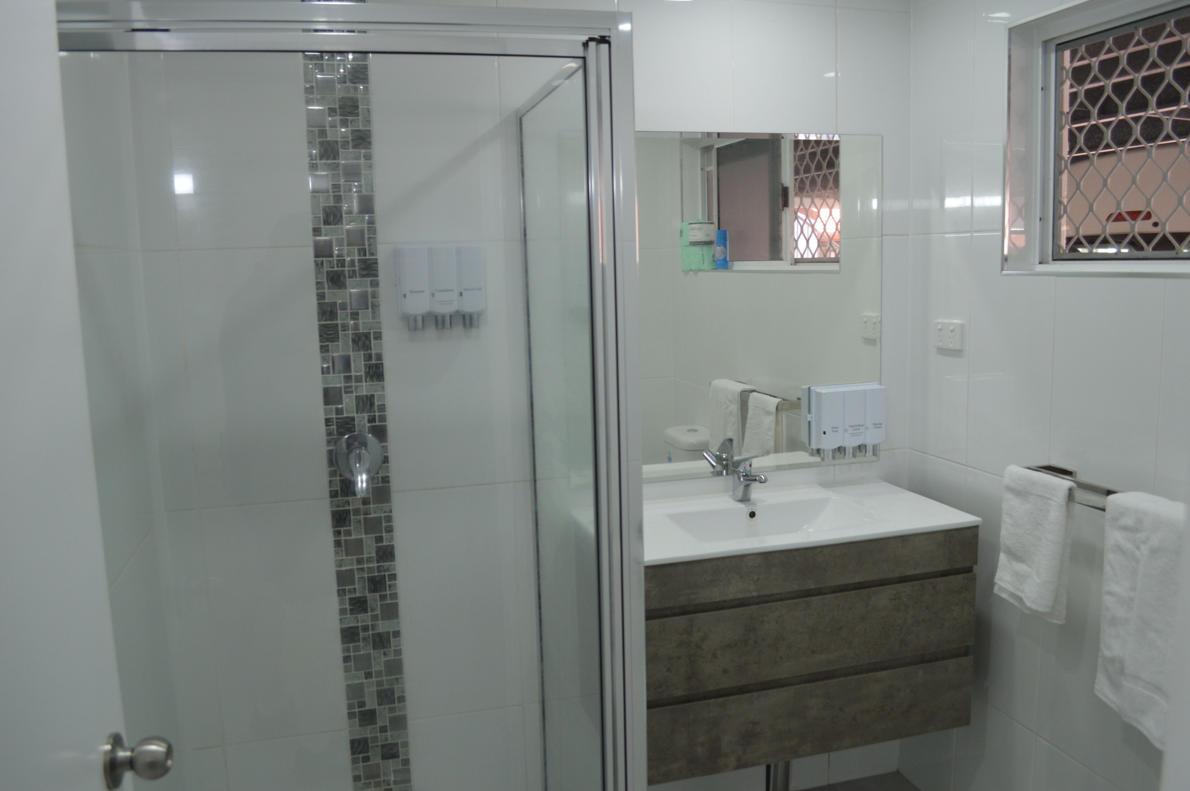 Une salle de bain avec une douche à parois de verre, un lavabo blanc avec un miroir au-dessus, et un porte-serviettes avec deux serviettes.