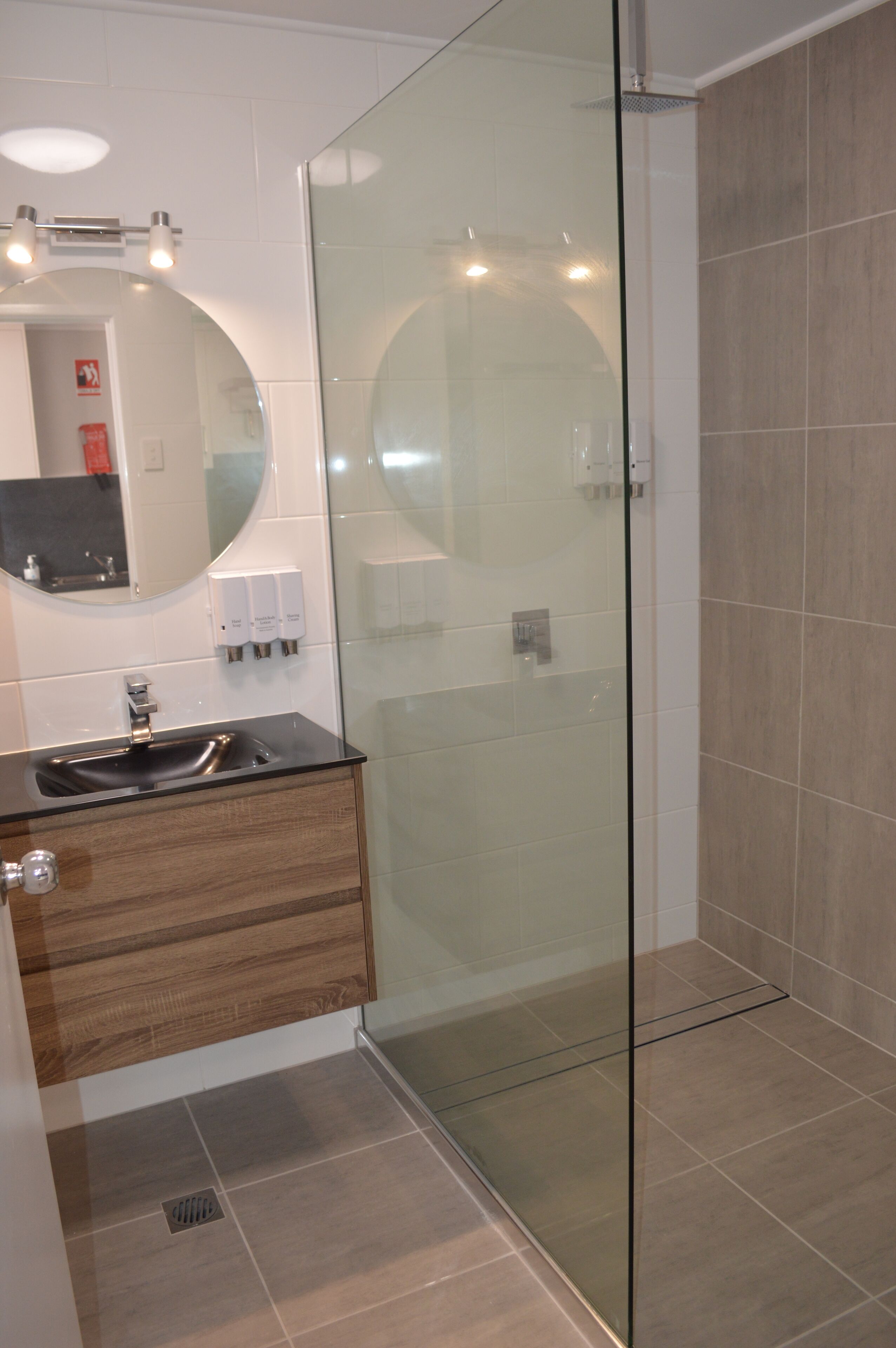 A modern bathroom with a glass shower enclosure, a wooden vanity with a sink, and a mirror above it.