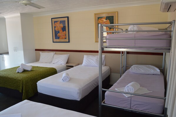 Habitación de hotel con tres camas individuales, cada una con cubrecama blanco y toallas enrolladas. Hay dos cuadros florales enmarcados en la pared.