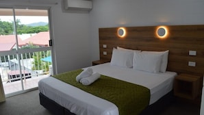 A hotel room with a bed, a green blanket, white pillows, and a wooden headboard with circular light fixtures. - Monte Carlo Motor Inn (Rosslea)