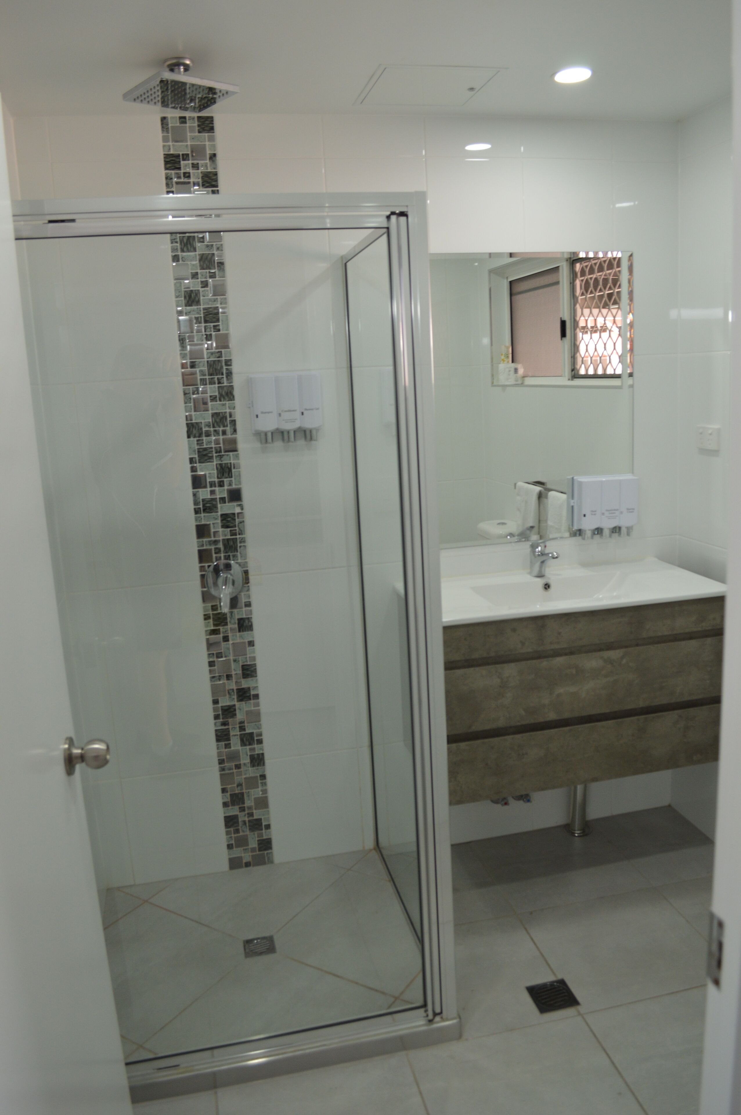 A modern bathroom with a glass-enclosed shower, a sink with a mirror, and a tiled floor.