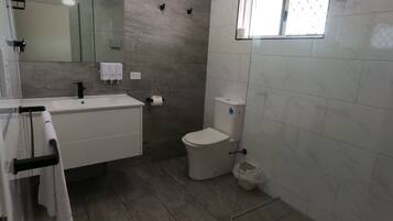 A bathroom with a white sink, mirror, and toilet. There is a window above the toilet and a towel rack with towels.