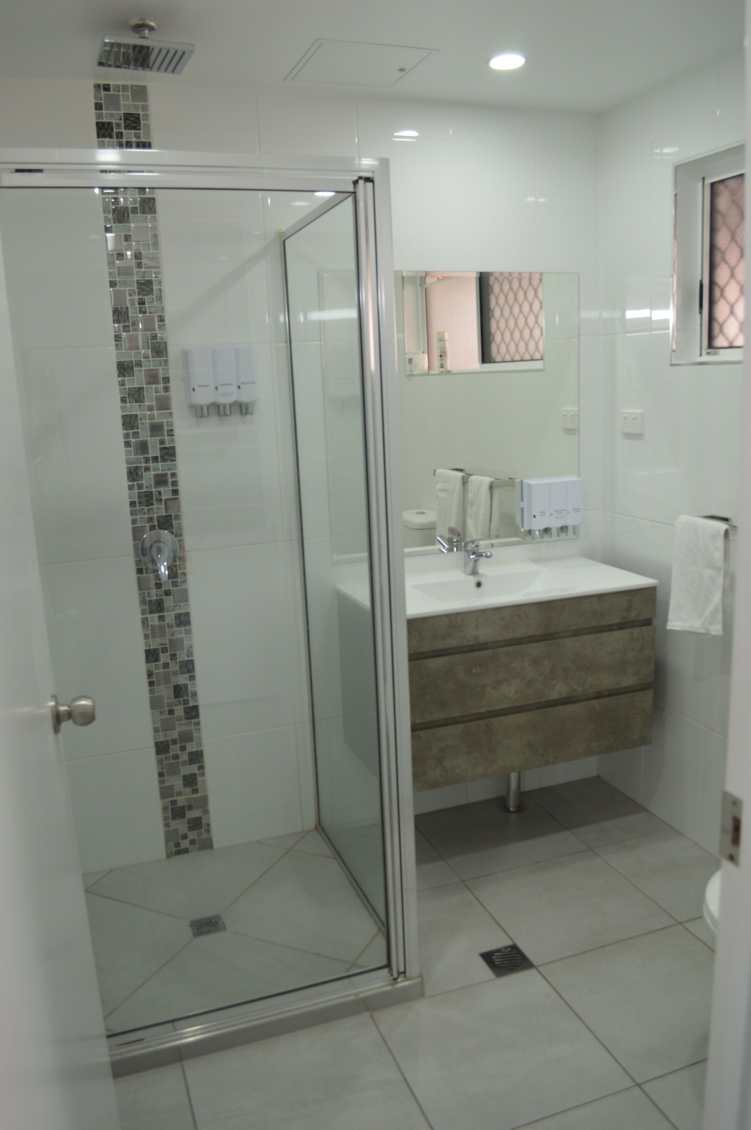 Une salle de bain moderne avec une douche à parois de verre, un lavabo avec un miroir et un sol carrelé.