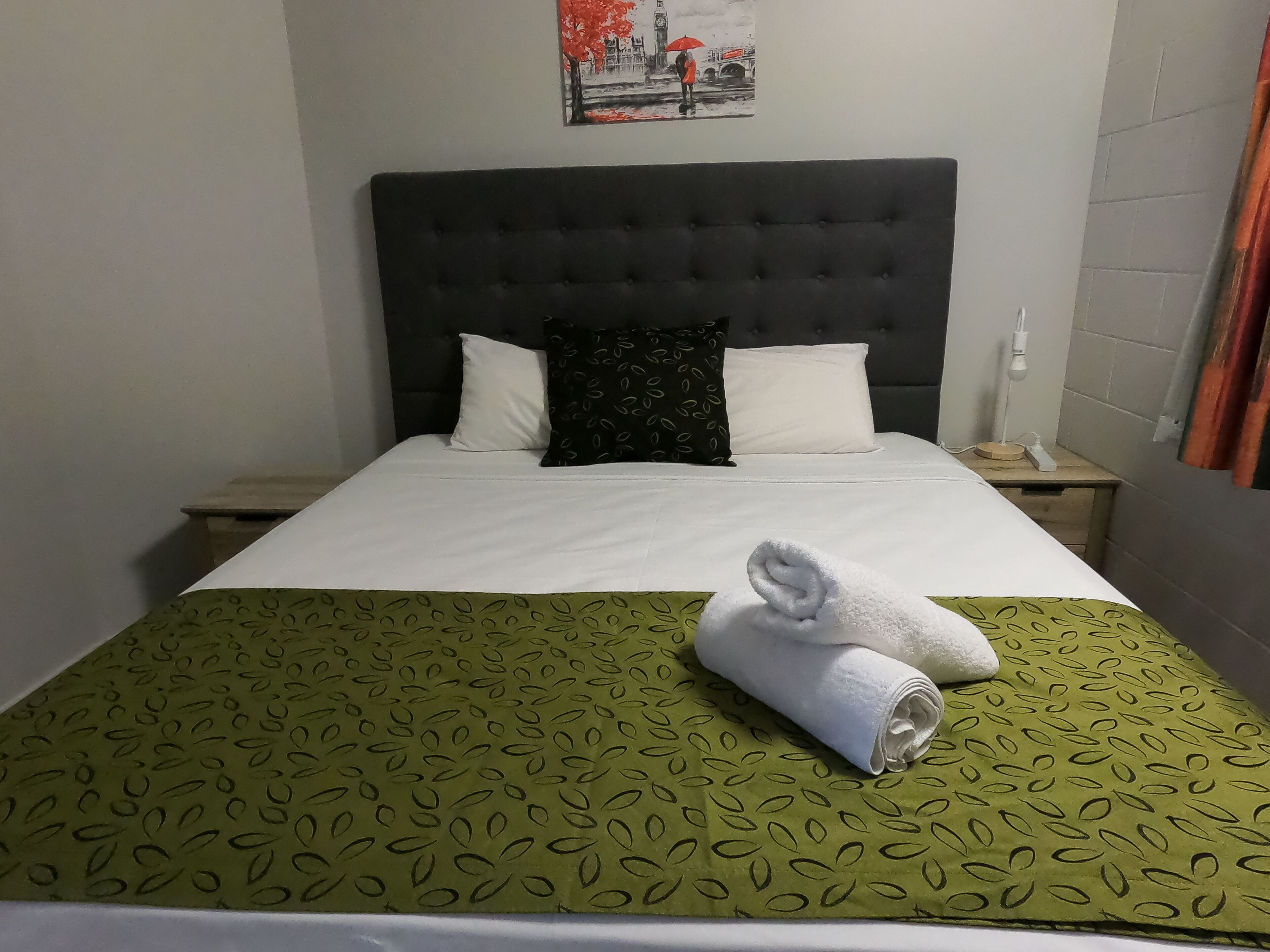 A neatly made bed with a green patterned bedspread, white pillows, and a rolled white towel on the bed.
