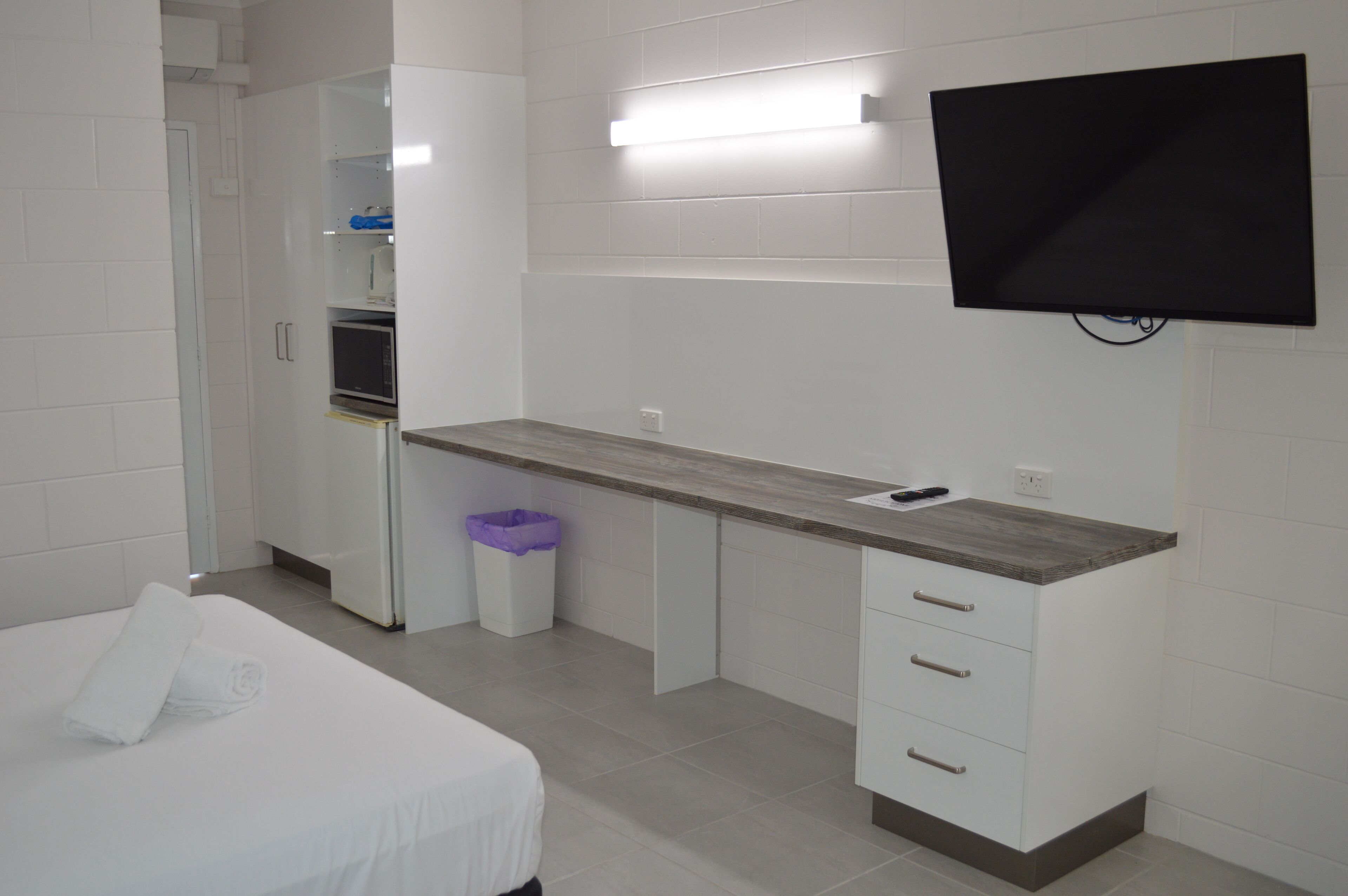 Ein Hotelzimmer mit Bett, Schreibtisch mit Schubladen, Mülleimer, Mikrowelle und Wand-Fernseher.
