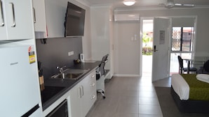 A compact kitchen with modern appliances, a dining area with a table and chairs, and a bedroom with a bed and a window. - Monte Carlo Motor Inn (Rosslea)