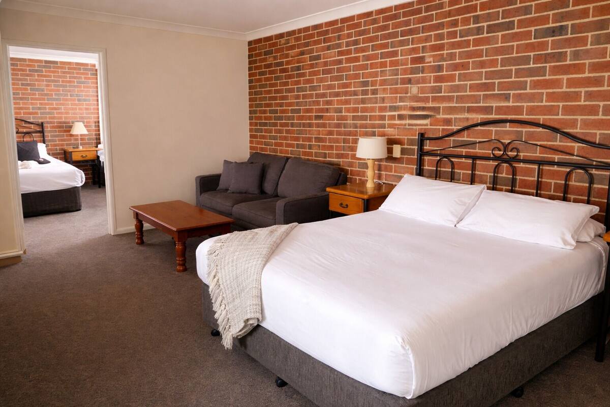 A bedroom with a bed, a sofa, a nightstand, and a lamp.