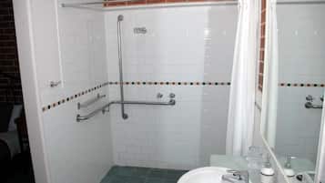 Ein Badezimmer mit weiß gefliesten Wänden, einem grünen Boden, einem weißen Waschbecken, einem Spiegel und einer Duschkabine mit Glastür.