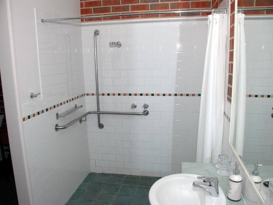 Ein Badezimmer mit weiß gefliesten Wänden, einem grünen Boden, einem weißen Waschbecken, einem Spiegel und einer Duschkabine mit Glastür.