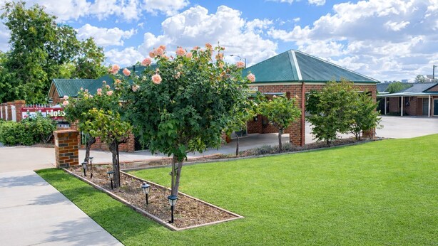 A building with a green roof, brick walls, and a well-maintained lawn. - Poachers Paradise Motel (Rutherglen)