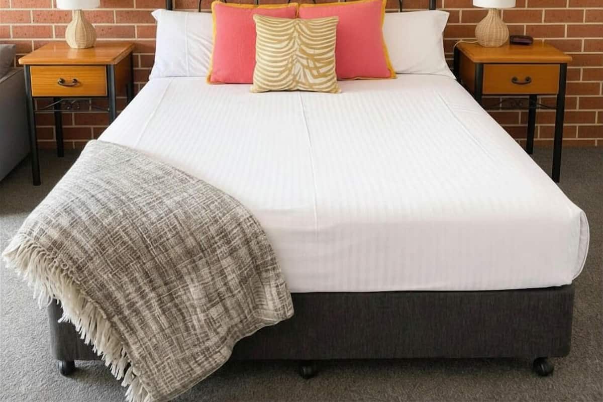 A bed with a headboard, two bedside tables, and a blanket.
