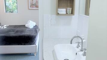 Une salle de bain moderne avec un lavabo blanc, un miroir et une étagère en bois où sont rangés les articles de toilette.
