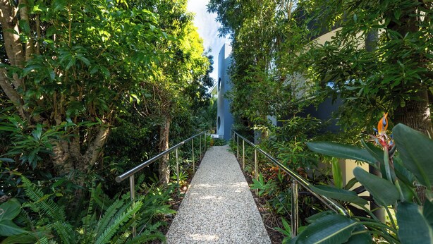 A pathway flanked by lush greenery and a modern building structure. - Noosa River Sandy Shores (Noosaville)