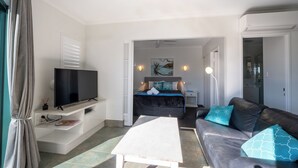 A modern living room with a flat-screen TV, a sofa, a coffee table, and a bed with a view of the sea. - Noosa River Sandy Shores (Noosaville)