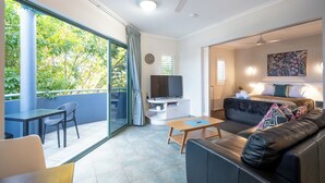 A modern living room with a sofa, a TV, and a dining area with chairs. - Noosa River Sandy Shores (Noosaville)