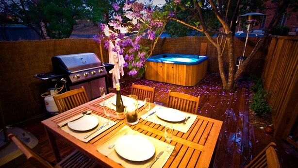 A wooden deck with a table set for two, a hot tub, and a grill. - The Old Parkes Convent (Parkes)