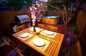 Um deck de madeira com mesa posta para dois, ofurô e churrasqueira.