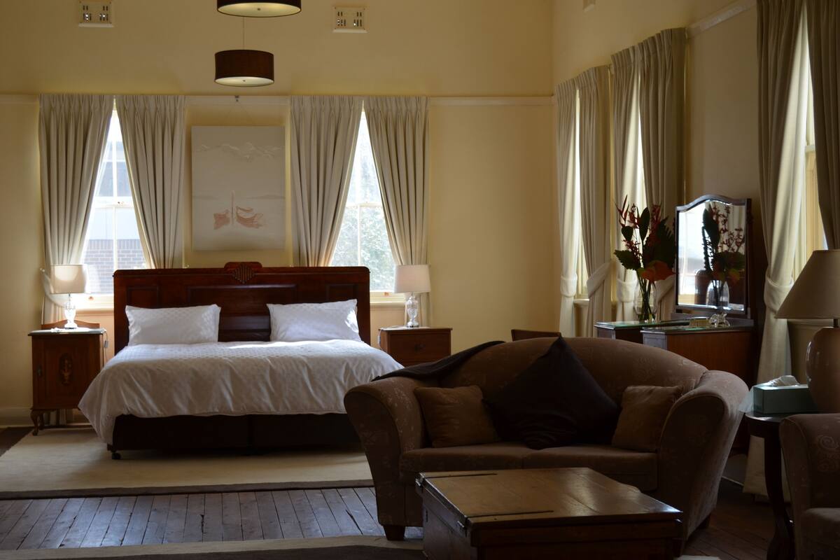 Una habitación de hotel con una cama grande, un sofá, una mesita y un escritorio con lámpara.