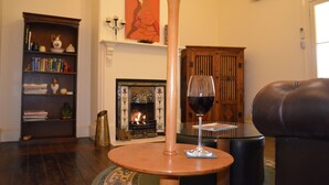 A cozy living room with a fireplace, a bookshelf, a leather armchair, and a glass of red wine on a small table. - The Old Parkes Convent (Parkes)