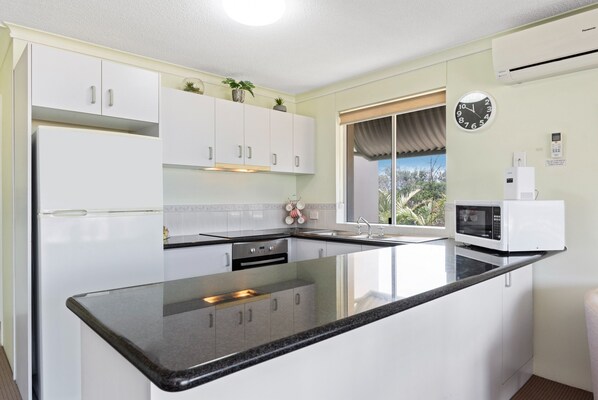 A modern kitchen with white cabinets, a black countertop, and a microwave. - Surfcomber on the Beach (Maroochydore)