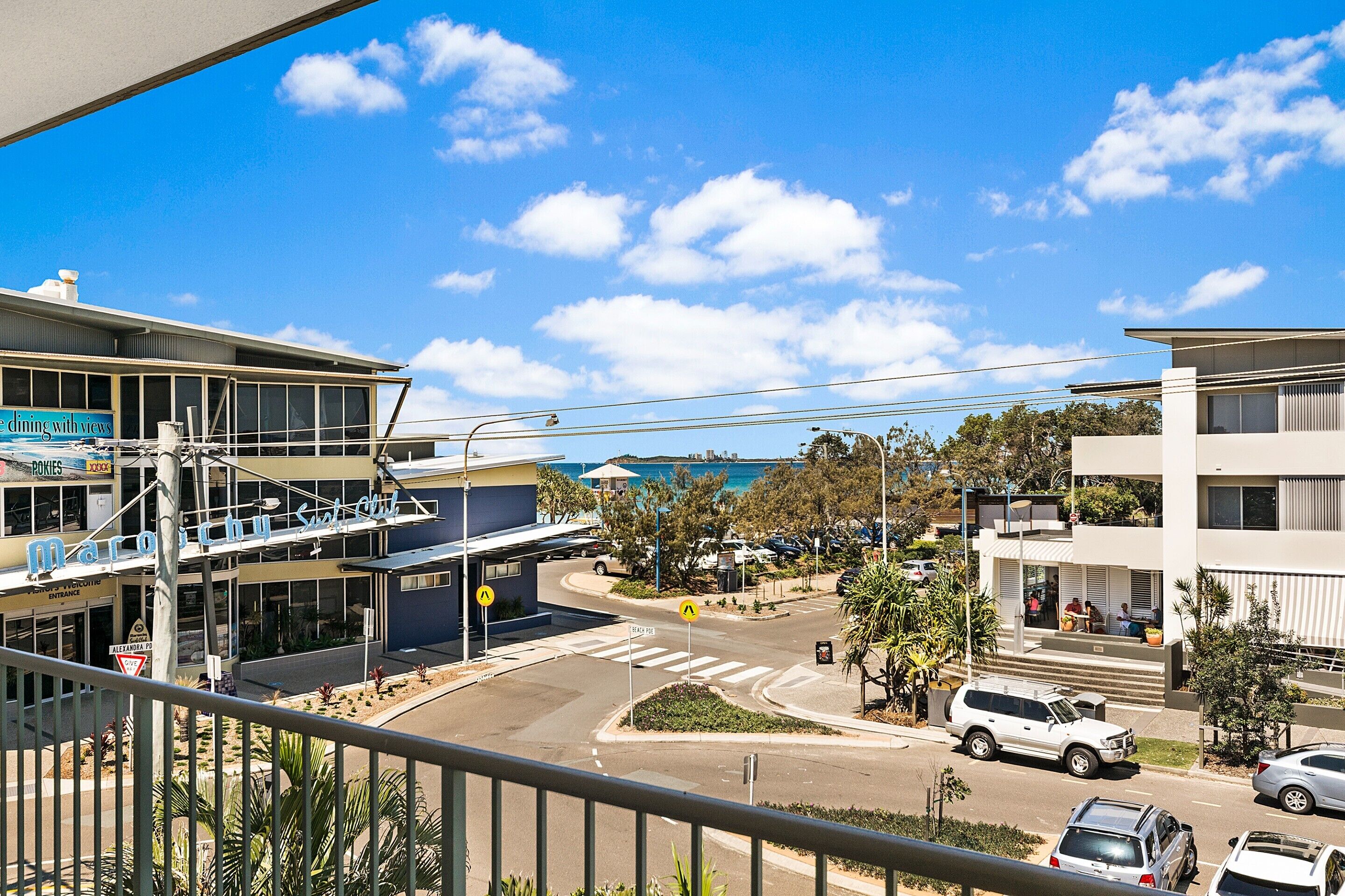 A coastal street view with buildings, a pedestrian crossing, and a clear blue sky.