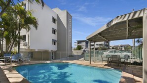 Une piscine dotée d’une zone couverte, entourée d’une clôture, et située à côté d’un bâtiment comportant de nombreuses fenêtres et des balcons.