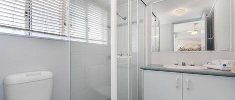 A bathroom with a toilet, a glass-enclosed shower, and a sink with a mirror above it.