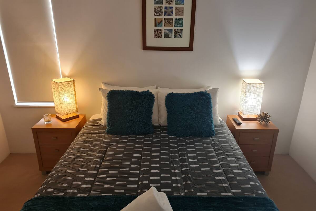 A neatly arranged bedroom with a bed, two bedside tables, and two wall-mounted lamps.