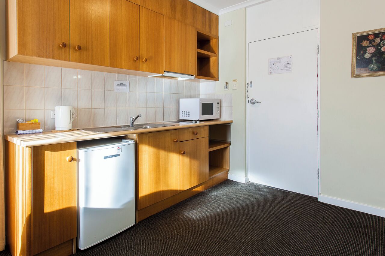 A compact kitchen with wooden cabinets, a microwave, a small refrigerator, and a sink.